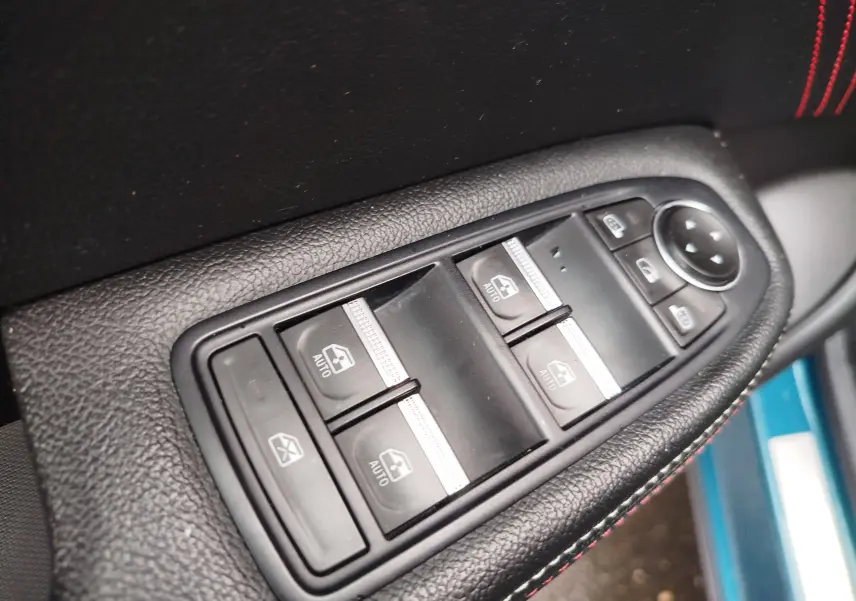 Gros plan sur les commandes de lève-vitres et rétroviseurs côté conducteur du Renault Arkana bleu Zanzibar, avec surpiqûres rouges.