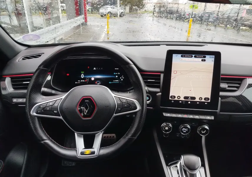 Vue intérieure centrée sur le volant et le tableau de bord du Renault Arkana 1.6 E-Tech, avec écran tactile et détails rouges.