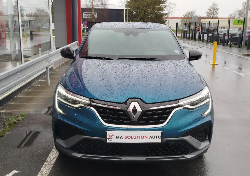 Vue frontale d'un Renault Arkana bleu Zanzibar 2022 sous la pluie, avec ses phares LED allumés et calandre noire distinctive.
