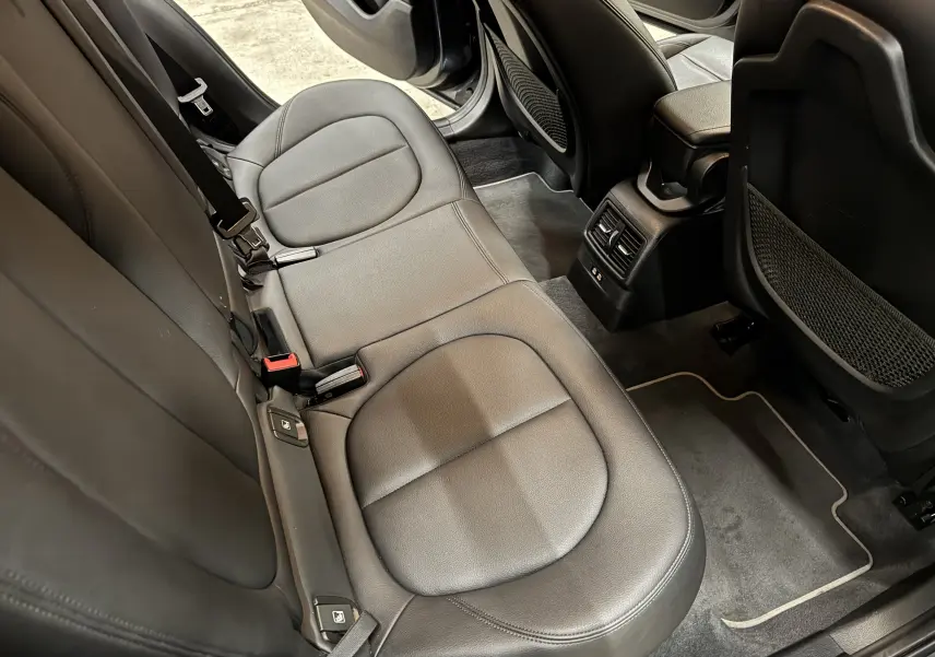 Vue intérieure de la banquette arrière en cuir noir d’une BMW X2 2019, avec tapis de sol velours et portes ouvertes.