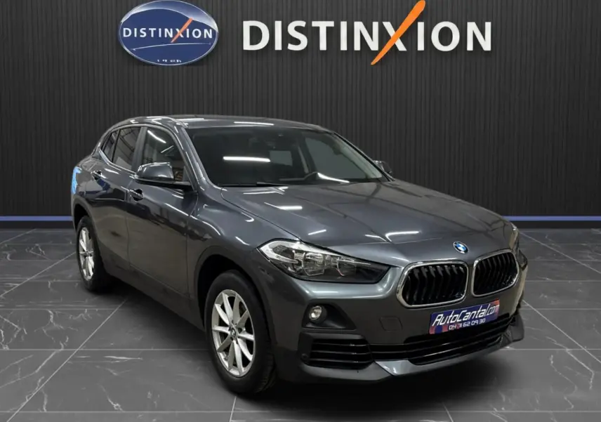 BMW X2 gris minéral métallisé vue 3/4 avant droit dans un showroom avec logo Distinxion en arrière-plan.