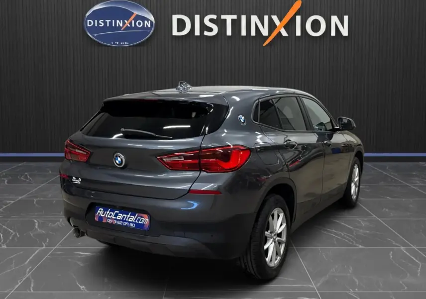 BMW X2 gris minéral métallisé vue 3/4 arrière droit, vitres surteintées et hayon fermé dans showroom.