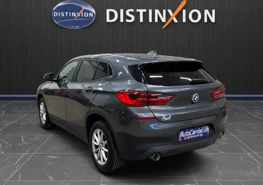 Vue 3/4 arrière droite d'un BMW X2 gris minéral métallisé avec vitres arrière surteintées dans un showroom.