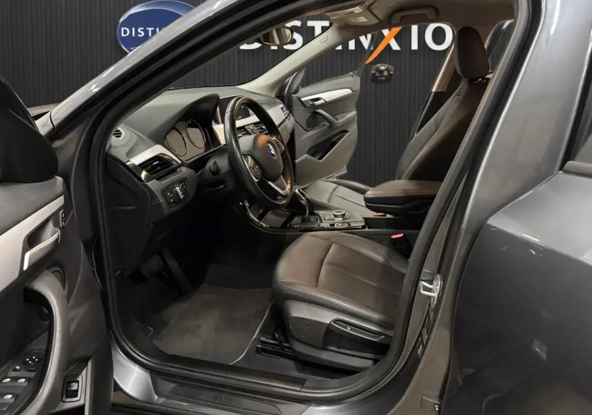 Vue intérieure côté conducteur d’un BMW X2 gris minéral métallique de 2019 avec sièges cuir noir et tableau de bord moderne.