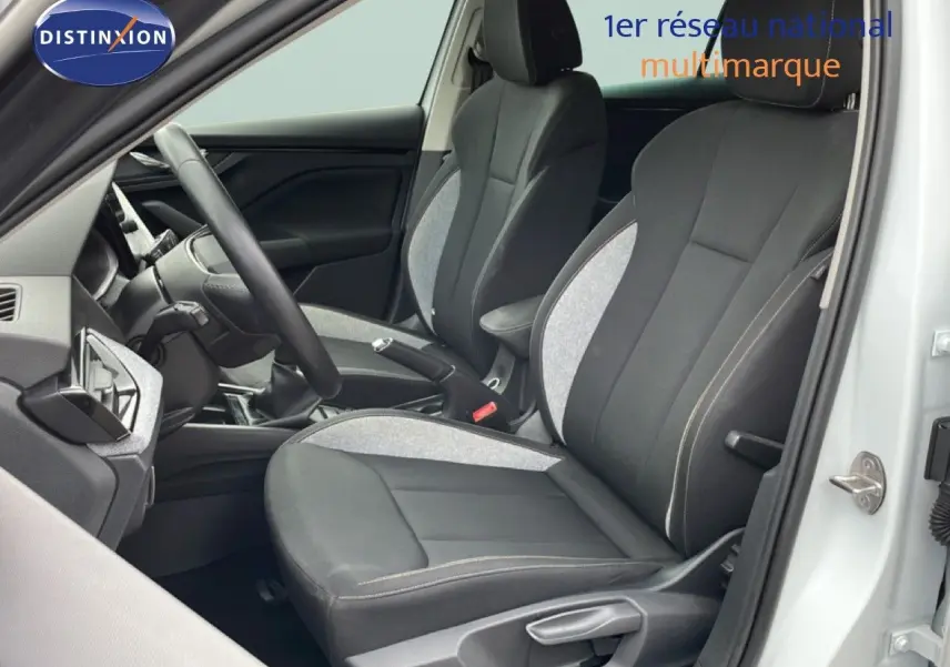Vue intérieure côté conducteur de la Skoda Scala blanc glacier, sièges tissu gris et noir avec volant cuir et boîte manuelle.