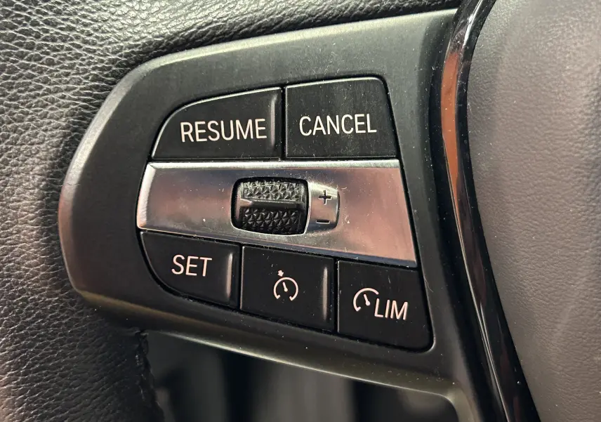 Gros plan sur les commandes de régulateur de vitesse au volant d'une BMW Série 1 noire 2023, version 16d.