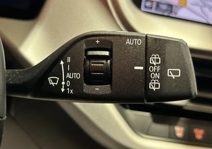 Gros plan sur la commande d'essuie-glace automatique de la BMW Série 1 noire 2023, avec écran GPS en arrière-plan.