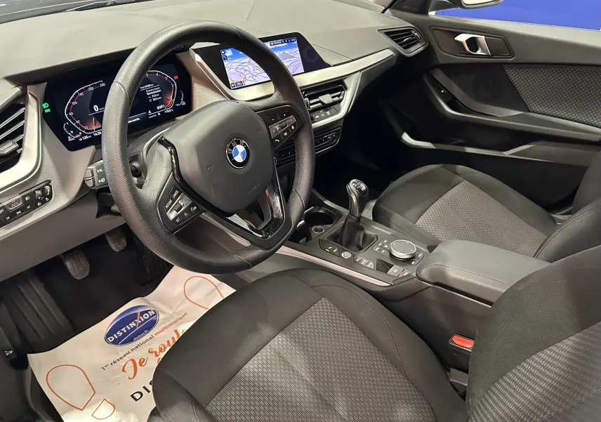 Vue intérieure côté conducteur de la BMW Série 1 noire 2023, avec tableau de bord digital et écran GPS intégré.