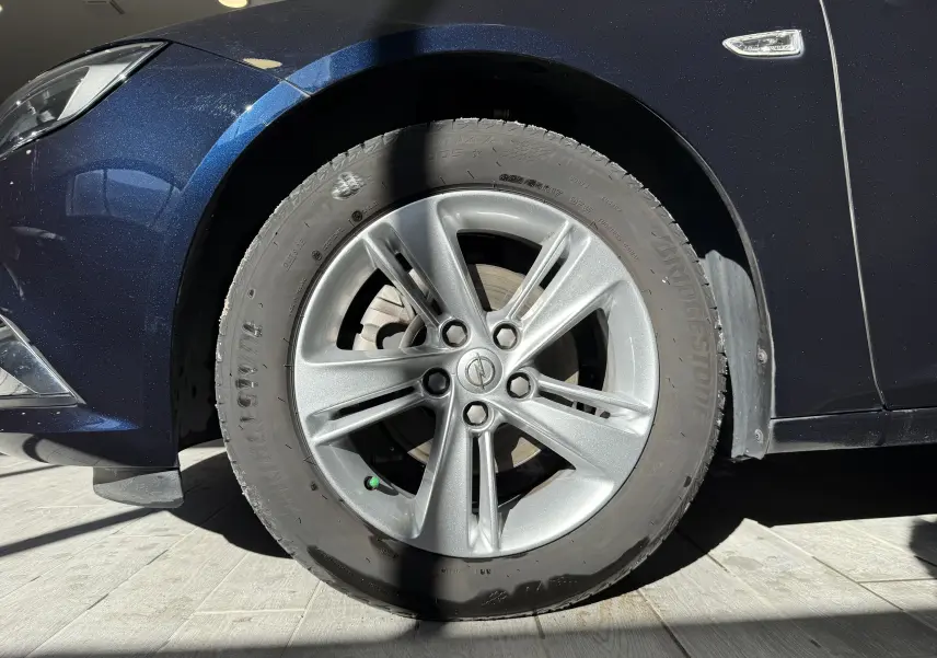 Gros plan sur la roue avant gauche d'une Opel Insignia Sports Tourer bleu lune marine métal avec jante alliage cinq branches.