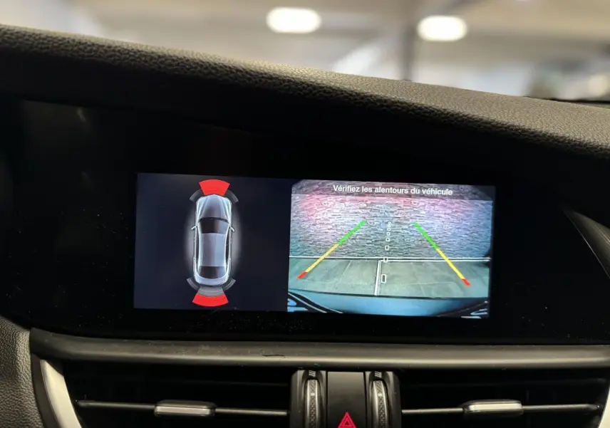 Écran intérieur de l'Alfa Romeo Giulia gris montrant la caméra de recul et l'aide au stationnement active.