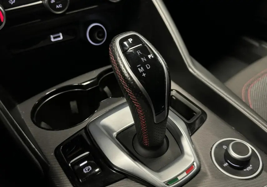 Gros plan sur la commande de boîte automatique avec surpiqûres rouges dans l’habitacle noir de l’Alfa Romeo Giulia gris 2021.