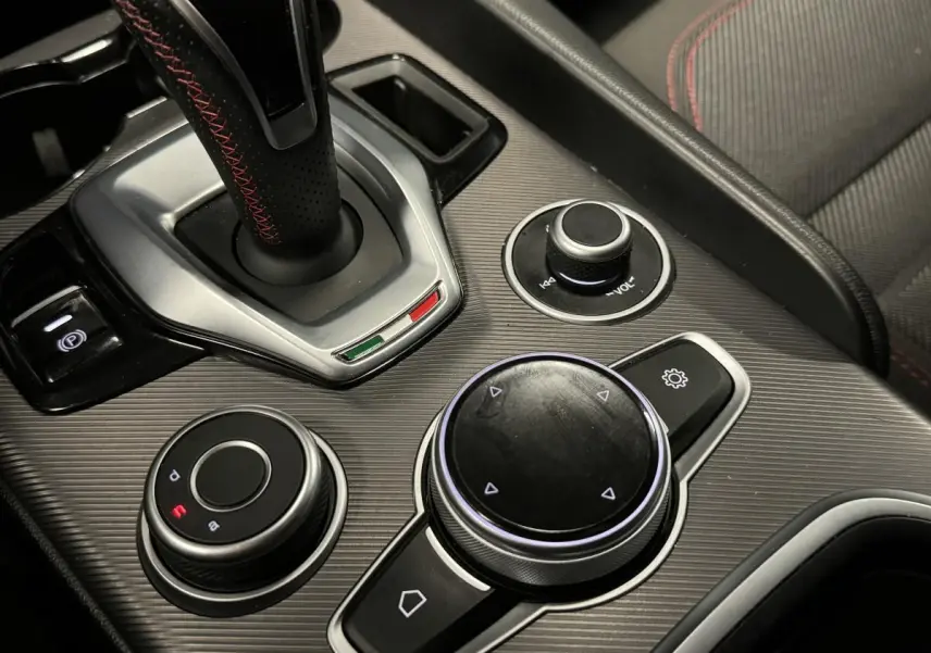 Gros plan sur la console centrale grise de l'Alfa Romeo Giulia 2.2 D 190 BVA Super avec sélecteur de mode et molette de contrôle.