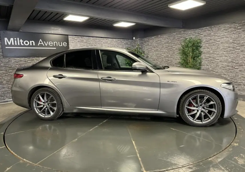 Vue latérale droite d'une Alfa Romeo Giulia gris métallisé avec jantes alliage 18 pouces Aero Scuro en intérieur showroom.