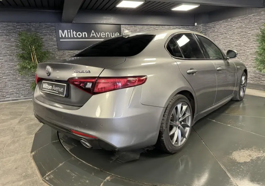 Vue 3/4 arrière droite d'une Alfa Romeo Giulia gris métallisé avec jantes alliage 18 pouces Aero Scuro dans un showroom.