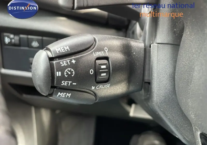 Gros plan sur la commande de régulateur de vitesse à gauche du volant dans l’habitacle noir du Citroën C5 Aircross bleu Eclipse Metal.