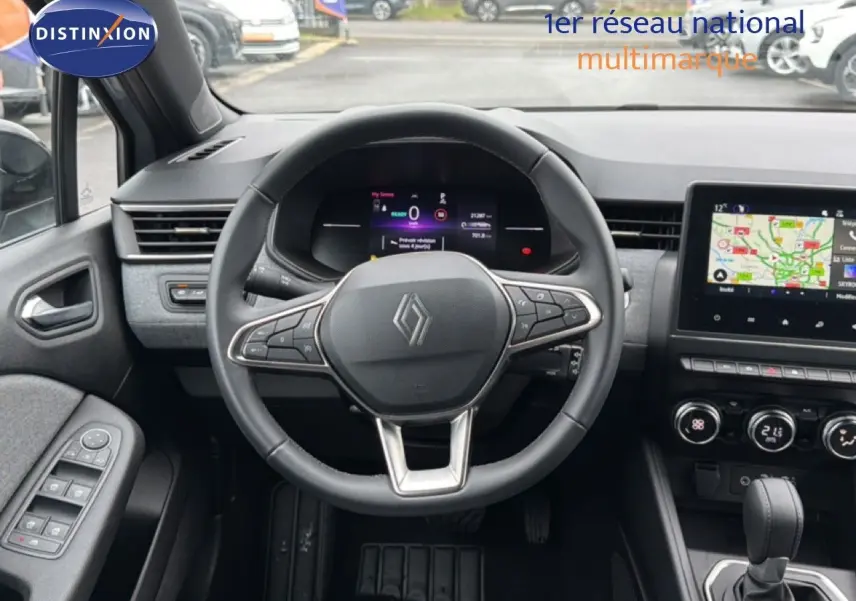 Vue intérieure centrée sur le volant et le tableau de bord de la Renault Clio gris Rafale, avec écran tactile et commandes visibles.