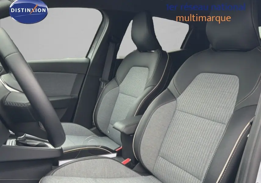 Vue intérieure côté conducteur de la Renault Clio 2025, sièges gris clair avec surpiqûres contrastantes et volant cuir multifonction.