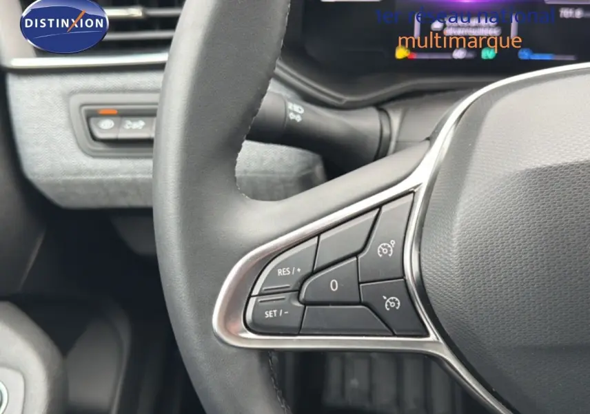 Gros plan sur le volant à droite de la Renault Clio 2025 gris Rafale Metal, avec commandes intégrées et tableau de bord flou en arrière-plan.