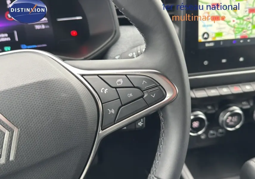 Gros plan sur le volant à droite de la Renault Clio 2025, avec commandes intégrées et tableau de bord numérique en arrière-plan.