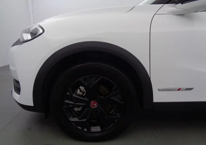Gros plan sur la roue avant gauche noire et la carrosserie blanche banquise d'un DS3 Crossback avec badge Performance Line.