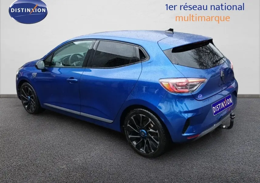 Vue 3/4 arrière gauche d'une Renault Clio 1.6 E-TECH hybride bleu Iron Metal avec jantes noires et attelage.
