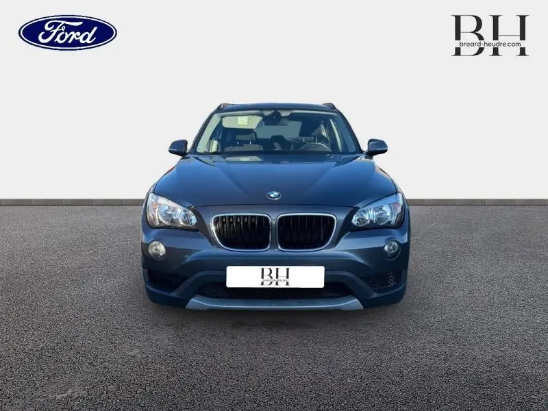 Vue avant d'un BMW X1 Mineralgrau 2013 avec calandre noire et phares halogènes allumés.