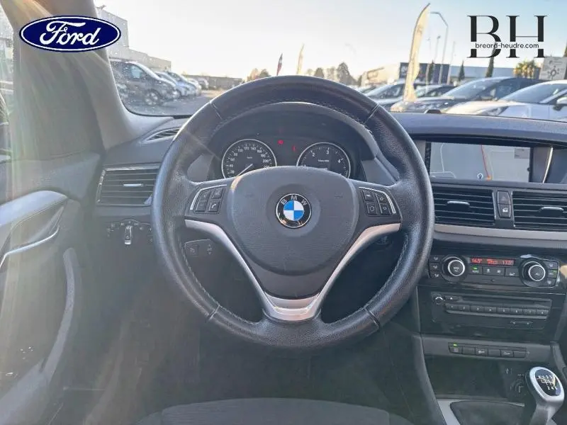 Vue intérieure centrée sur le volant cuir BMW avec commandes, tableau de bord et écran multifonction visibles.