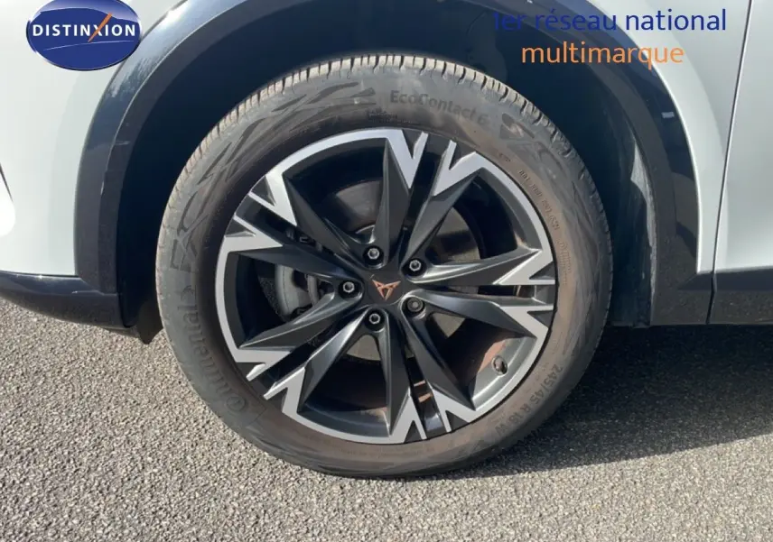 Gros plan sur la roue avant droite du CUPRA Formentor blanc neige métal, mettant en valeur la jante noire et argentée au design dynamique.
