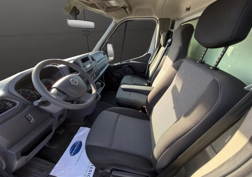 Vue intérieure côté conducteur du Nissan Interstar 2024, sièges gris et tableau de bord avec volant multifonctions.