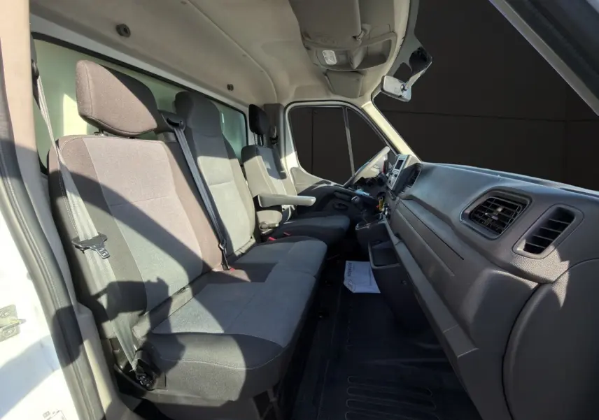 Vue intérieure côté conducteur du Nissan Interstar 2024 blanc, montrant les sièges gris et le tableau de bord noir.