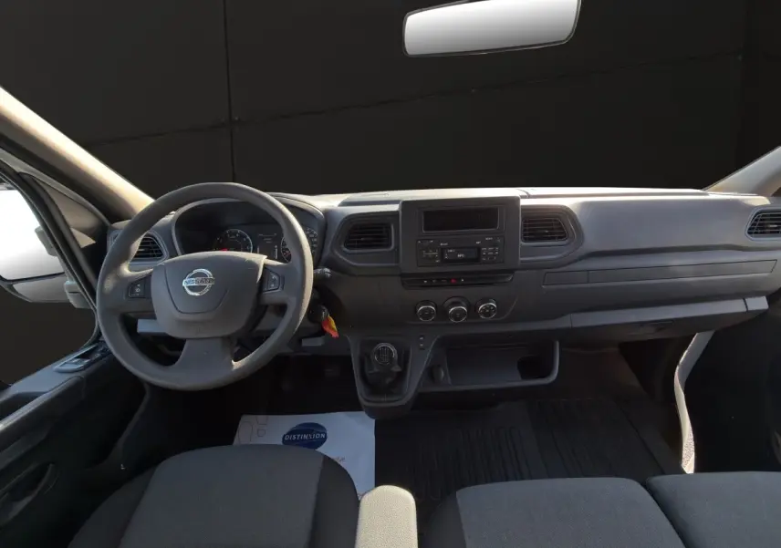Vue intérieure du tableau de bord et volant du Nissan Interstar 2024, avec commandes manuelles et écran central.