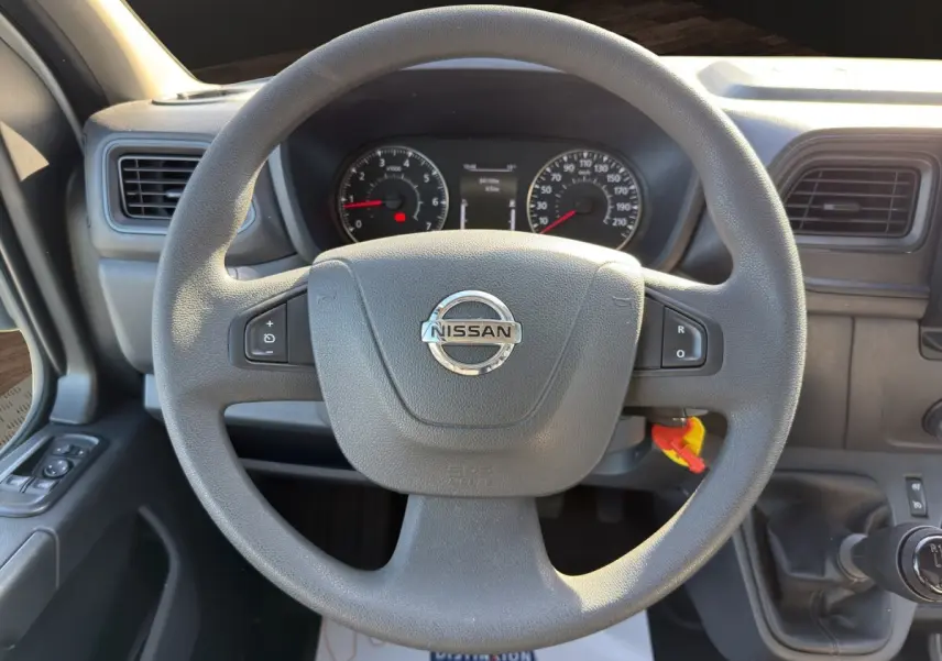 Vue centrée sur le volant multifonctions gris du Nissan Interstar 2024 avec tableau de bord et levier de vitesse manuel.