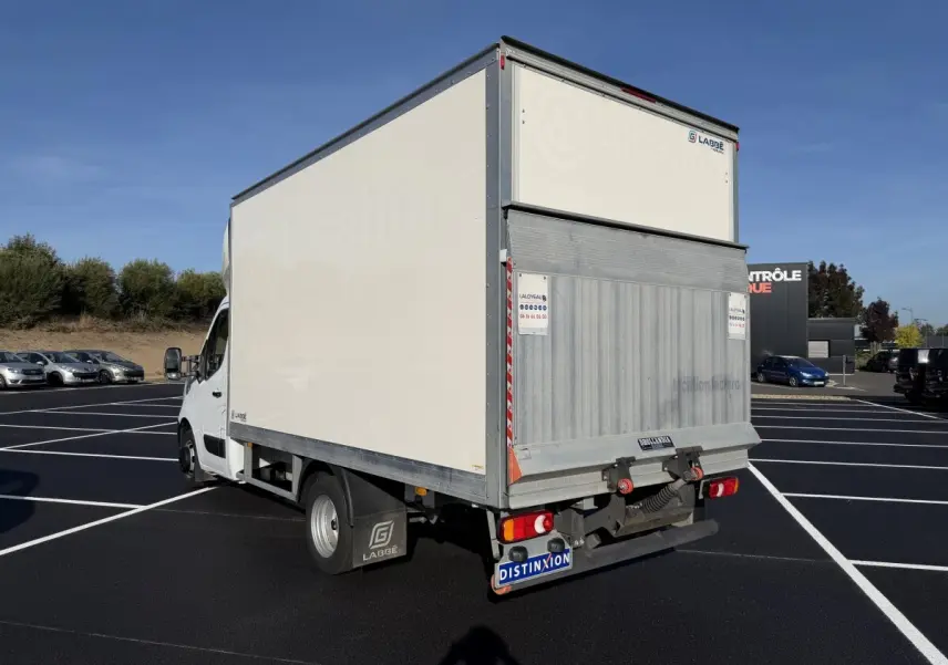Vue 3/4 arrière droite d’un utilitaire blanc Nissan Interstar avec caisse fermée et hayon métallique en parking.