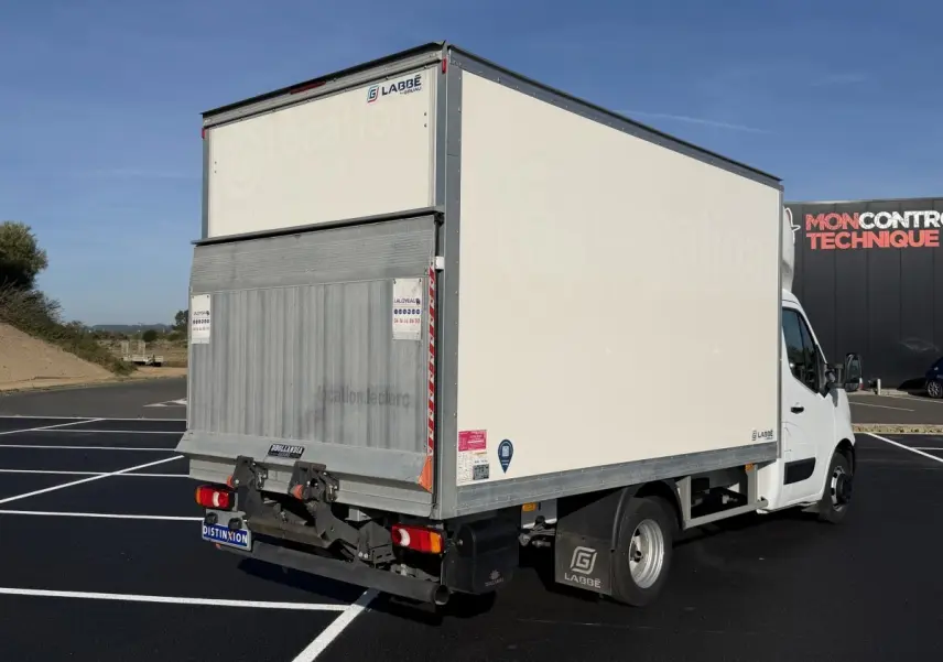 Vue 3/4 arrière droite d’un utilitaire blanc Nissan Interstar avec caisse fermée et hayon élévateur, stationné sur un parking.