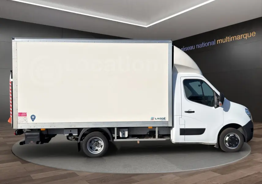 Vue latérale droite d’un utilitaire blanc Nissan Interstar avec caisse fermée et hayon, en intérieur showroom.