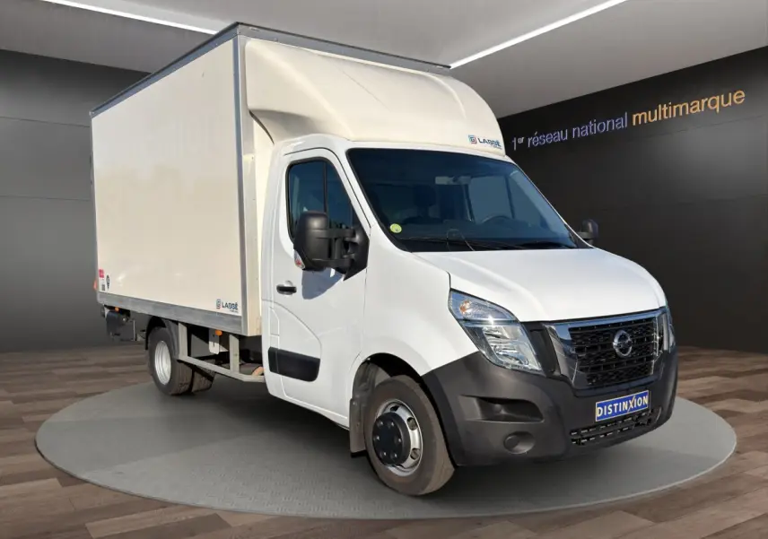 Vue 3/4 avant droit d’un utilitaire blanc Nissan Interstar avec caisse de livraison et hayon, sur fond neutre intérieur.