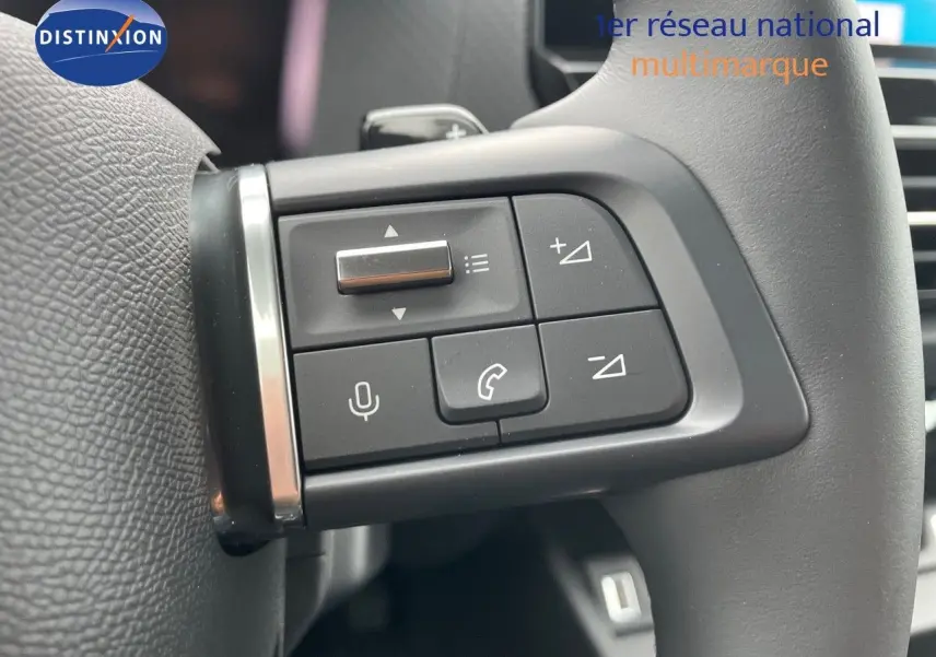 Gros plan sur les commandes du volant d'une Citroën C4 blanche métal 2024, mettant en valeur les boutons multifonctions.