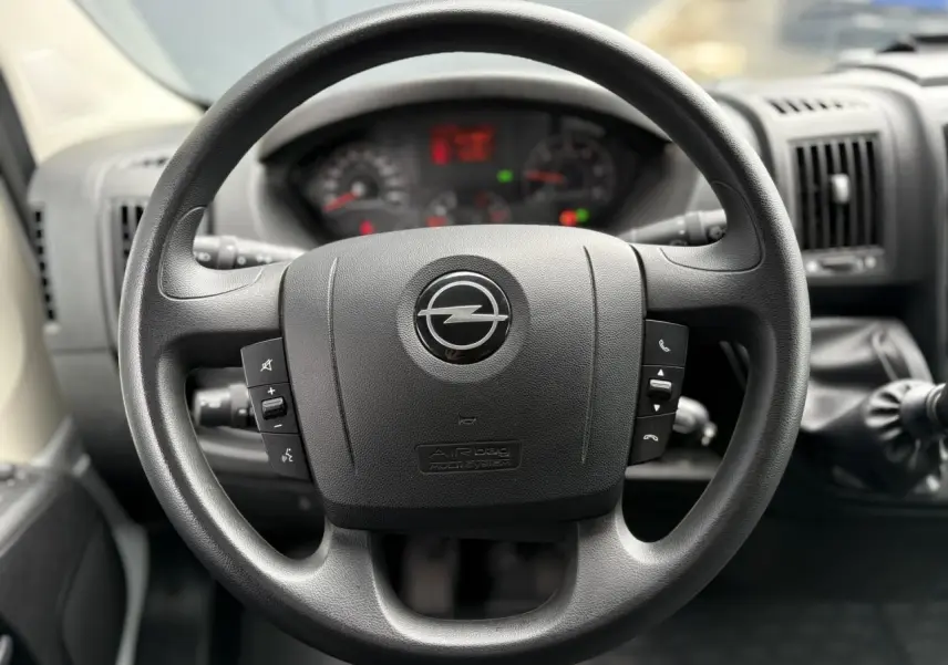Volant noir avec logo Opel au centre, vue rapprochée de l'intérieur du Movano Fourgon 2023, tableau de bord flou en arrière-plan.