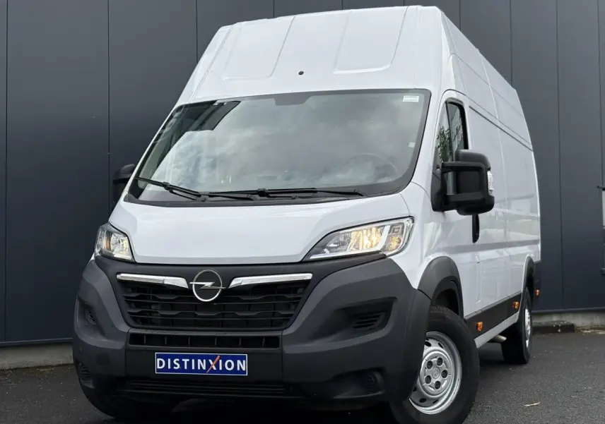 Opel Movano Fourgon blanc en 3/4 avant droit avec calandre noire et feux allumés sur fond urbain.