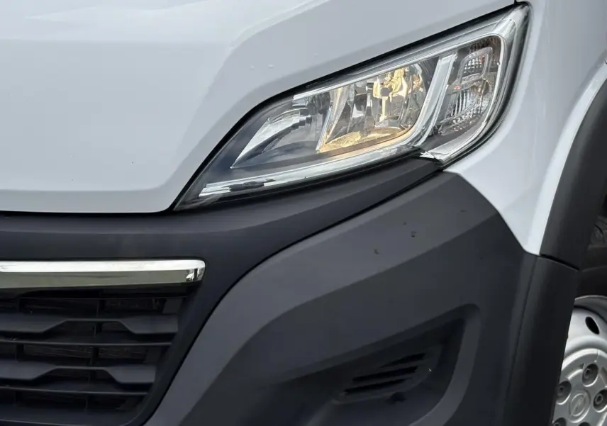 Gros plan sur le phare avant droit blanc de l'Opel Movano Fourgon 2023 avec calandre noire et jante acier visible.