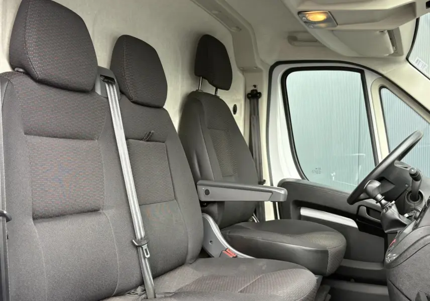 Intérieur avant du fourgon Opel Movano blanc, vue latérale sur les sièges noirs et le volant côté droit.