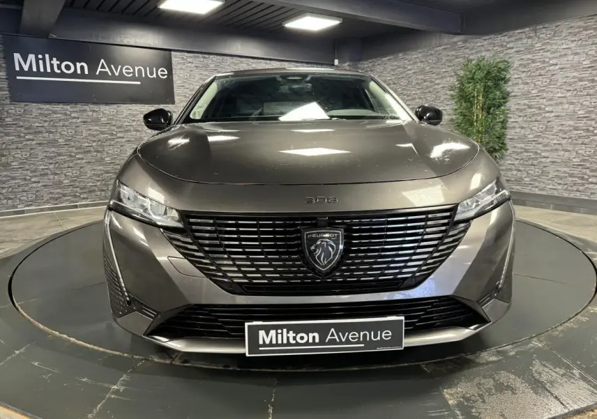 Vue frontale d'une Peugeot 308 SW gris métallisé avec calandre noire et logo lion central lumineux.