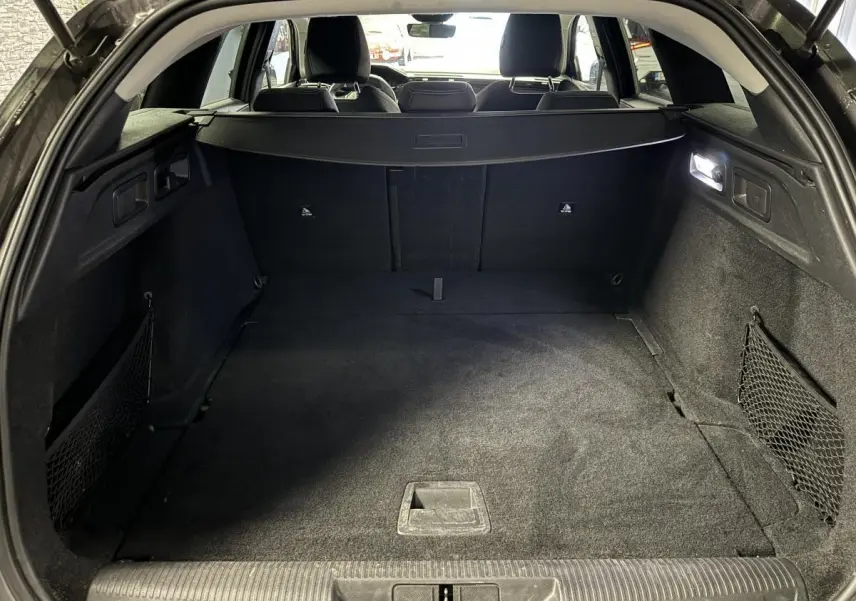 Coffre ouvert d'une Peugeot 308 SW gris, vue intérieure arrière montrant un espace de chargement propre et éclairé.