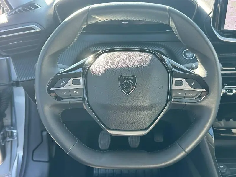 Vue rapprochée du volant cuir noir de la Peugeot 208 1.2 100ch Allure 2024, avec commandes intégrées et logo lion central.