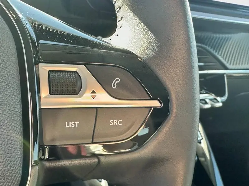 Gros plan sur les commandes du volant noir de la Peugeot 208 1.2 100ch S&S Allure 2024 avec boutons LIST et SRC visibles.