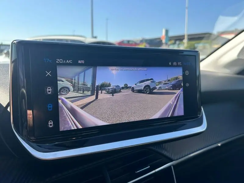 Affichage de la caméra de recul sur l'écran du tableau de bord d'une Peugeot 208 gris, montrant le parking derrière le véhicule.