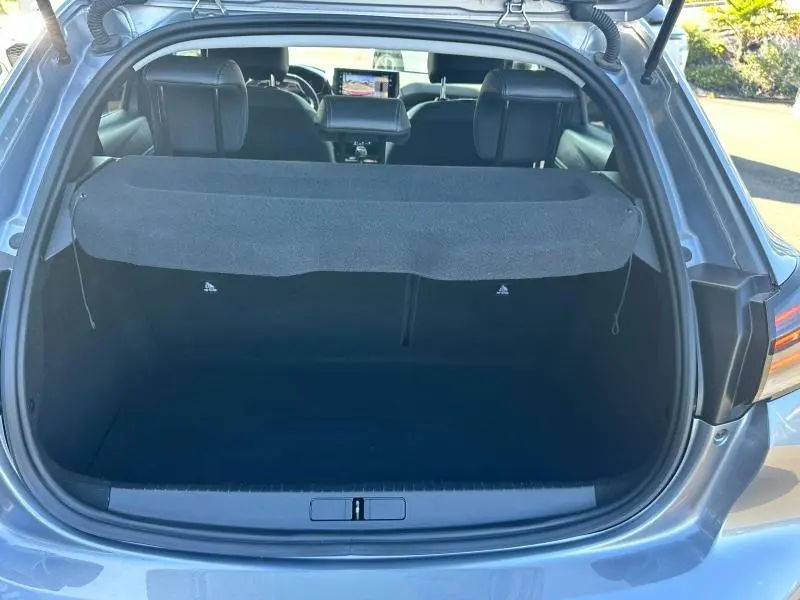 Coffre ouvert vu de l'arrière d'une Peugeot 208 gris 2024, montrant l'espace de chargement et l'intérieur des sièges arrière.