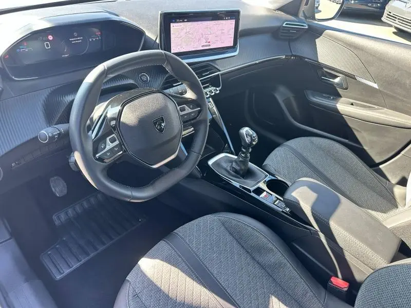 Vue intérieure côté conducteur de la Peugeot 208 1.2 100ch Allure 2024 grise, avec volant compact et écran tactile central.