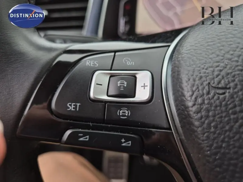 Gros plan sur les commandes du volant cuir multifonction du Volkswagen T-Roc gris, mettant en valeur les boutons d'assistance à la conduite.