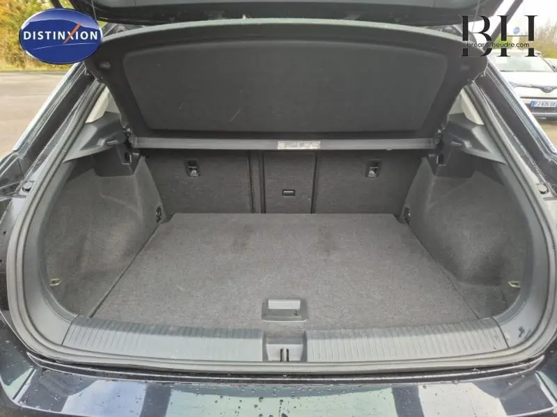 Coffre ouvert vu de l'arrière d'un Volkswagen T-Roc gris avec intérieur de coffre en tissu gris et cache-bagages relevé.